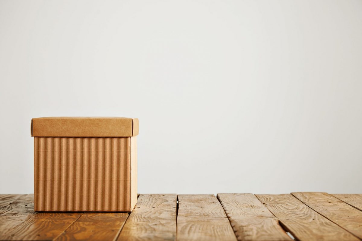 front shot unlabeled square beige cardboard box with cover wooden floor isolated white min