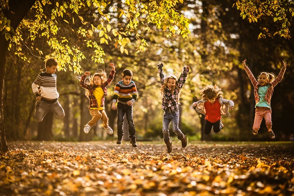 playful little friends having fun while jumping in autumn day at the park.